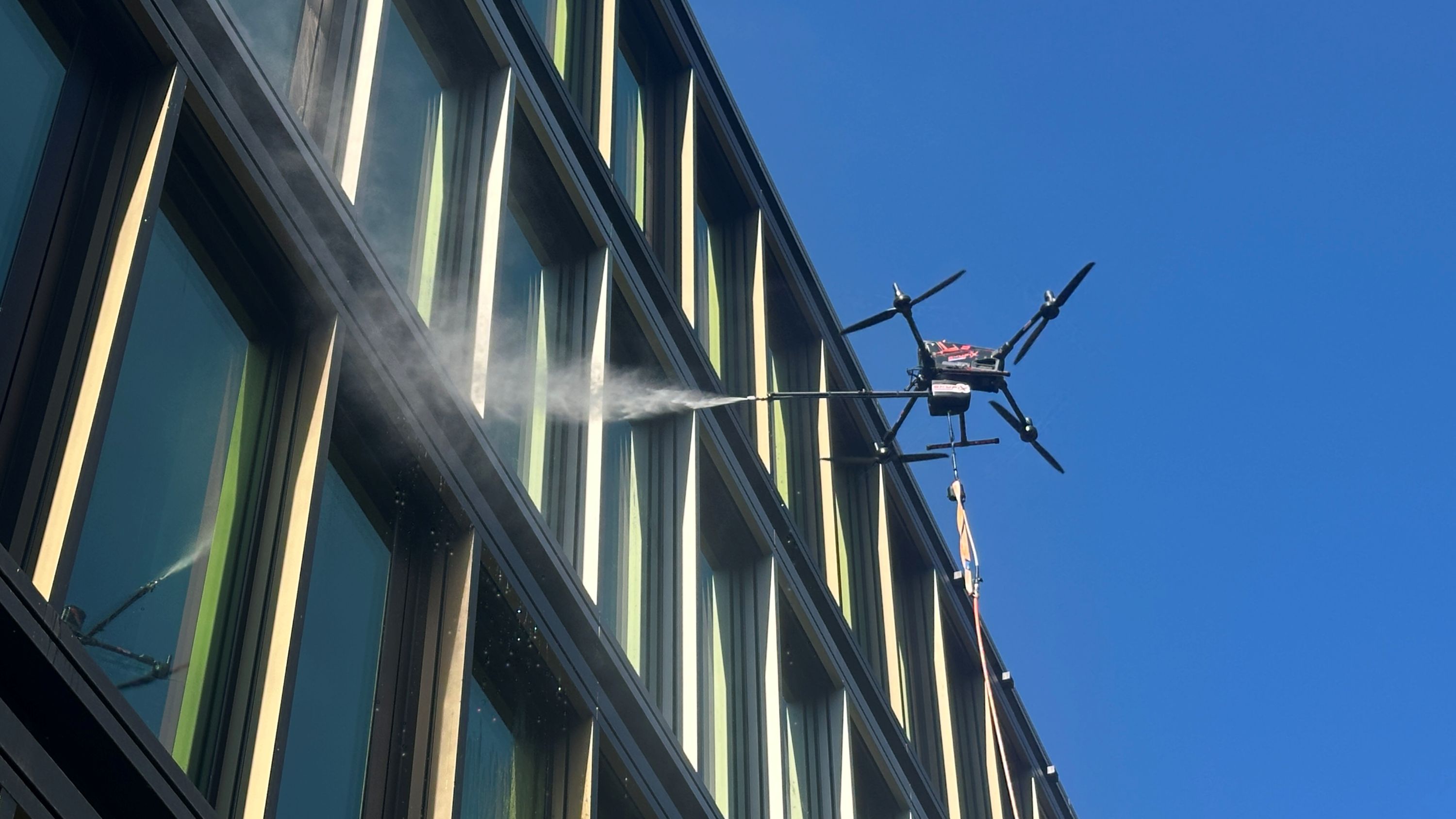 Die Reinigungsdrohne von skyXwash reinigt eine Glasfassade am PANDION Officehome Ostkreuz Campus in Berlin. Die KI-gestützte Systemlösung kommt ohne Gerüst oder Hubsteiger aus und arbeitet mit reinem Osmosewasser | BERLINboxx